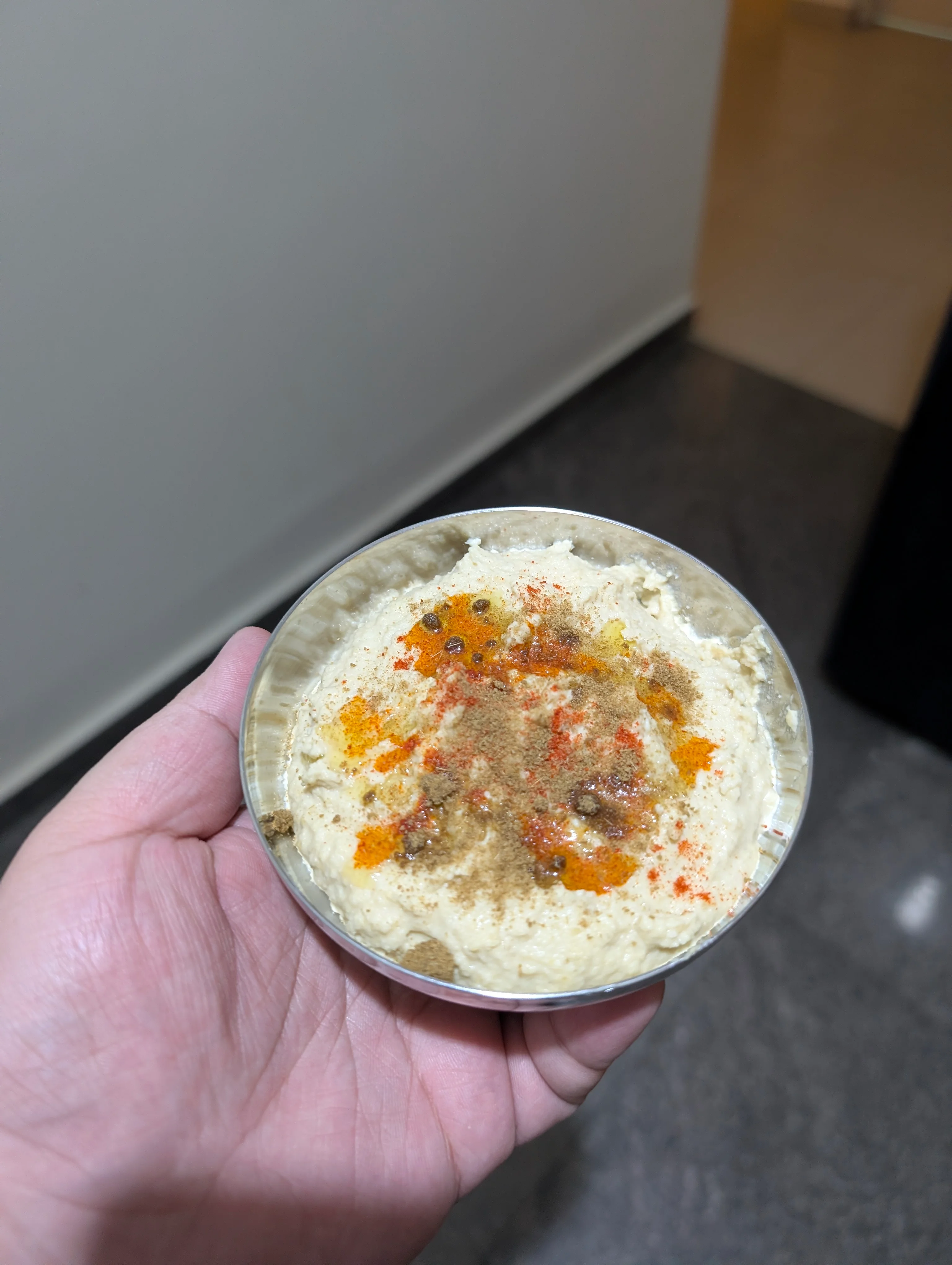 A small metal plate with some hummus that I've done a poor job of garnishing with some olive oil, red chilli powder and cumin powder.