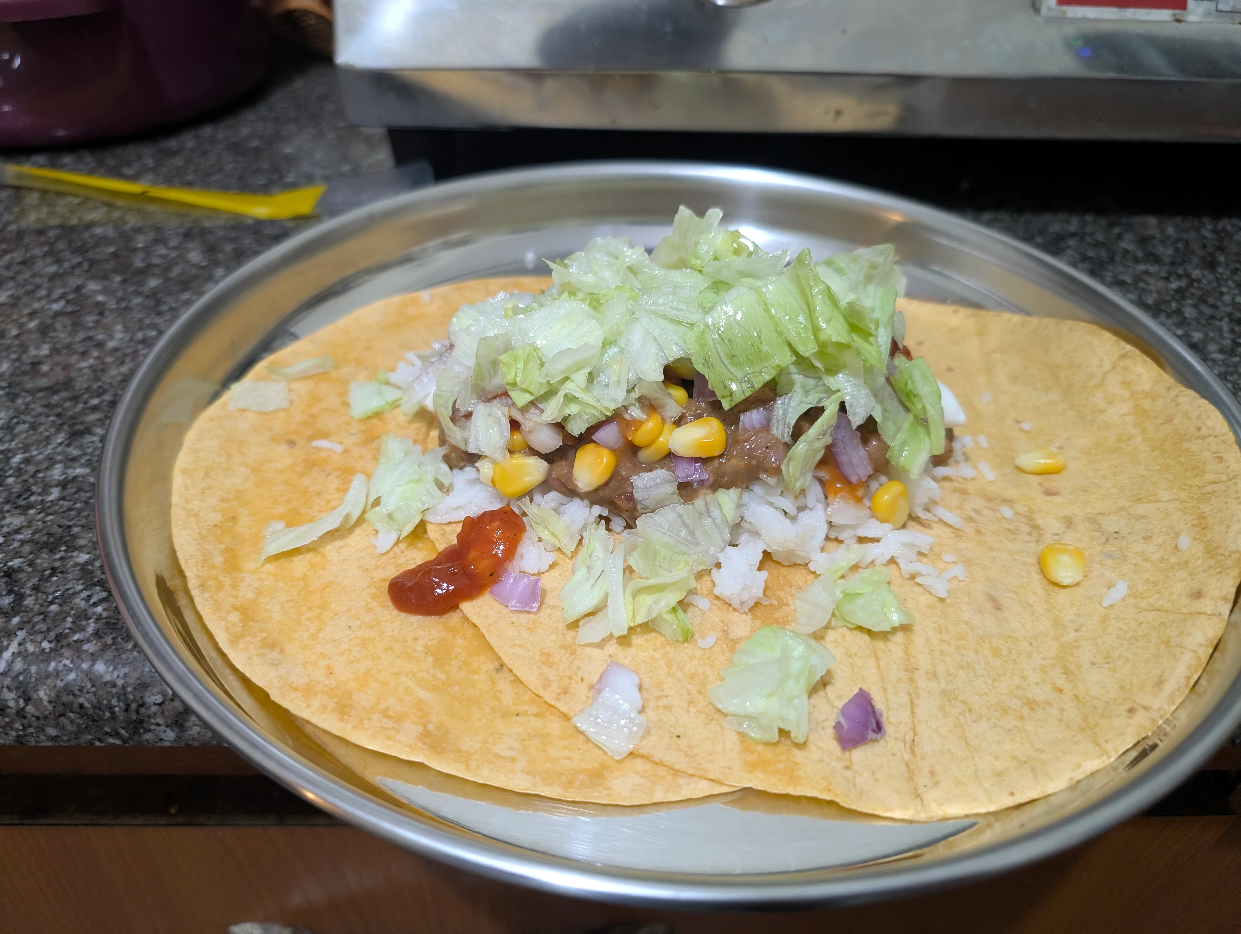 Two tortillas on a metal plate, overlapping around 30% with a big pile of fillings on top. The internet told me this is the right way to make a burrito with two wraps.
