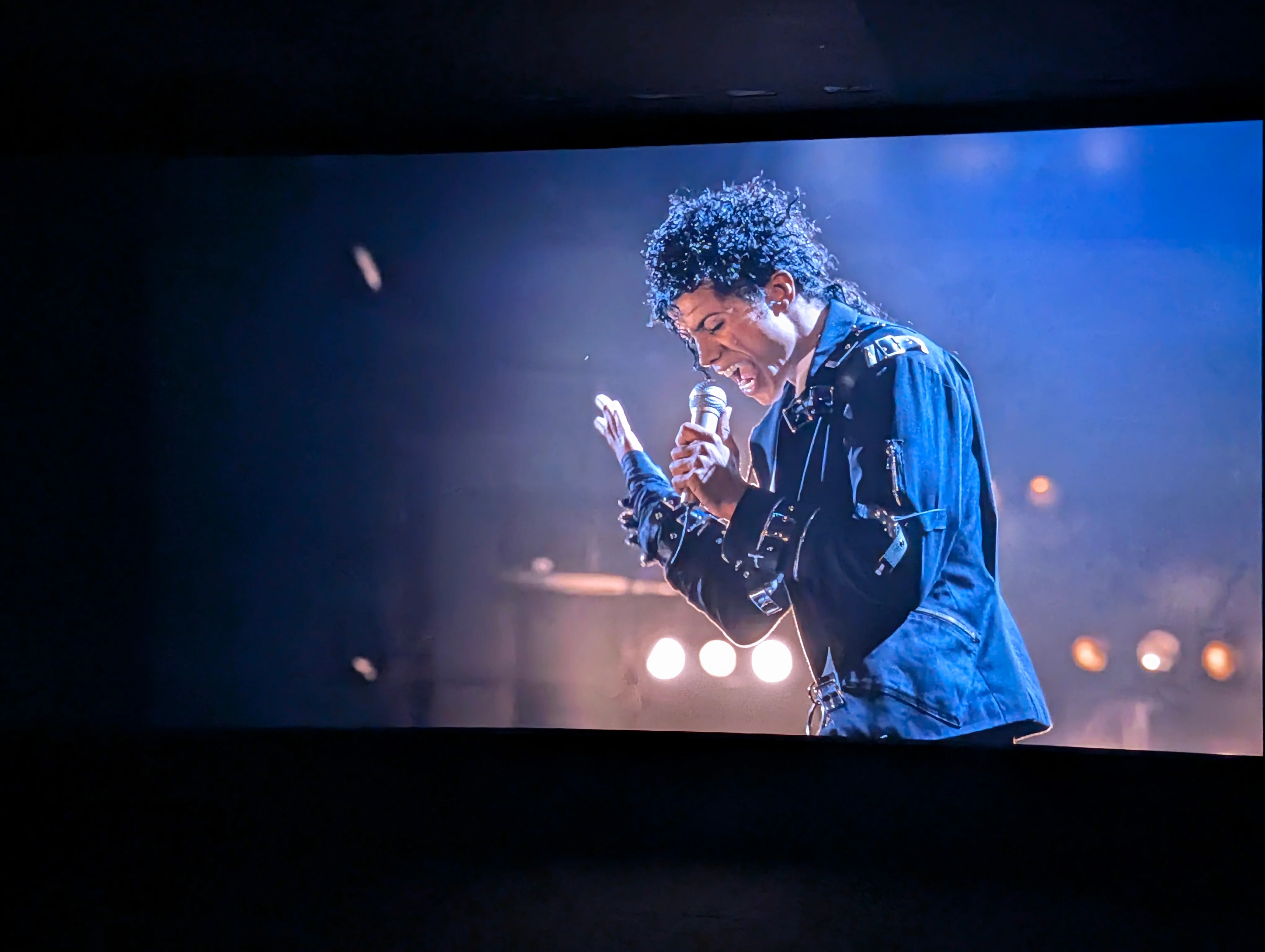 A scene from the movie Michael showing him singing on stage in a black jacket.