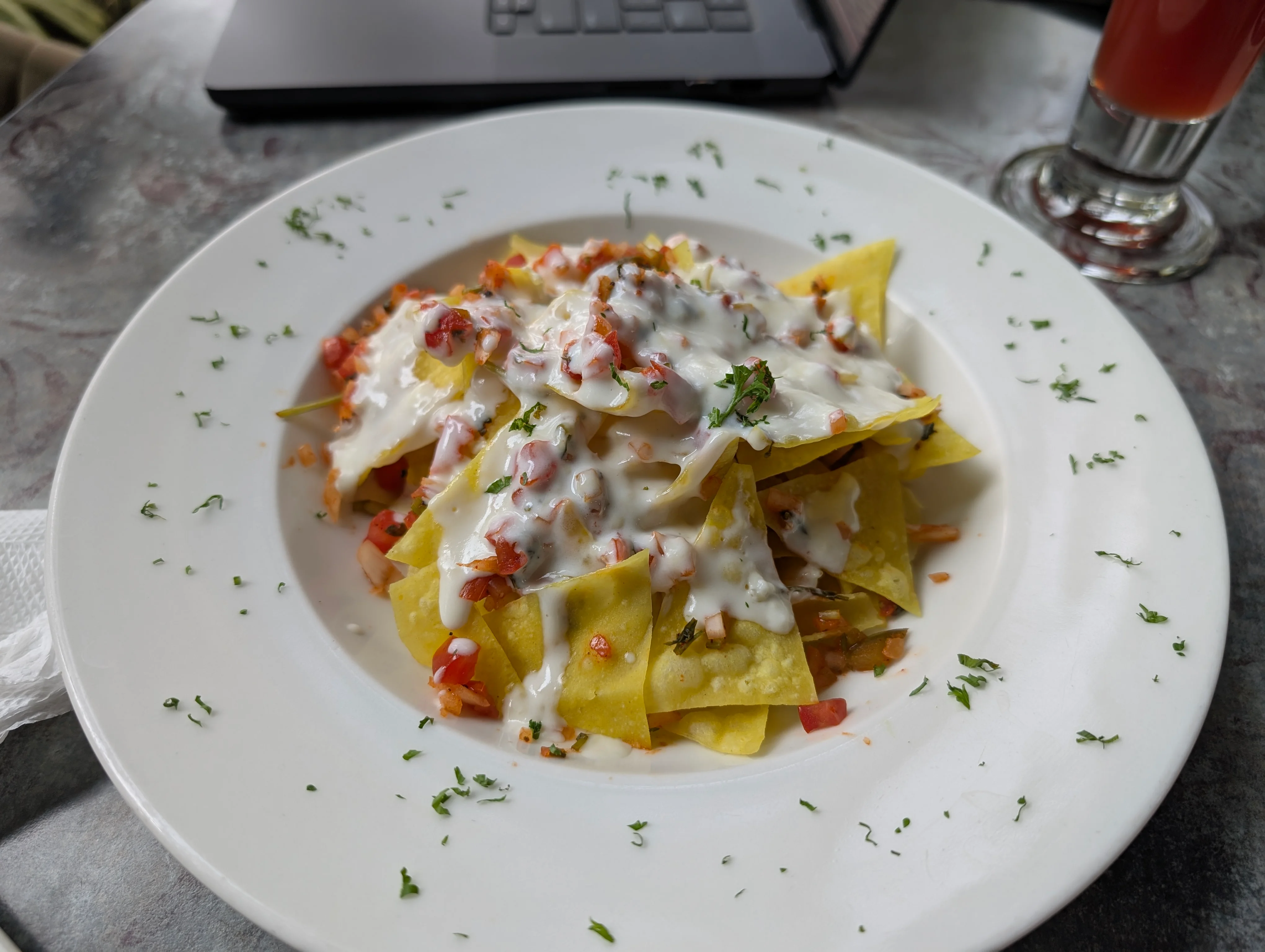 A white ceramic plate with a pile of nachos in the middle. There's melty white cheese all over the top.